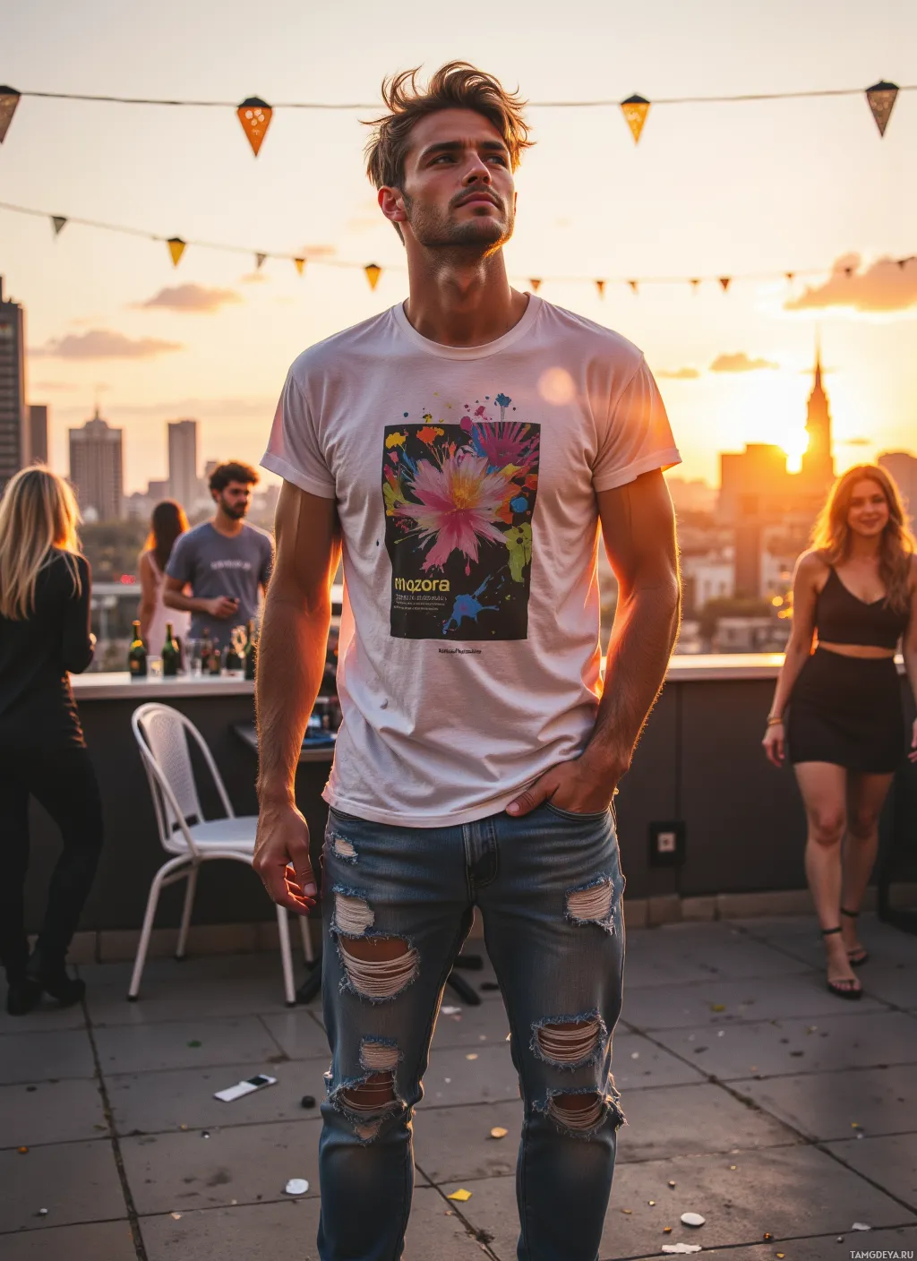 A man stands on a rooftop at sunset, wearing a white t-shirt and ripped jeans, with people in the background.
