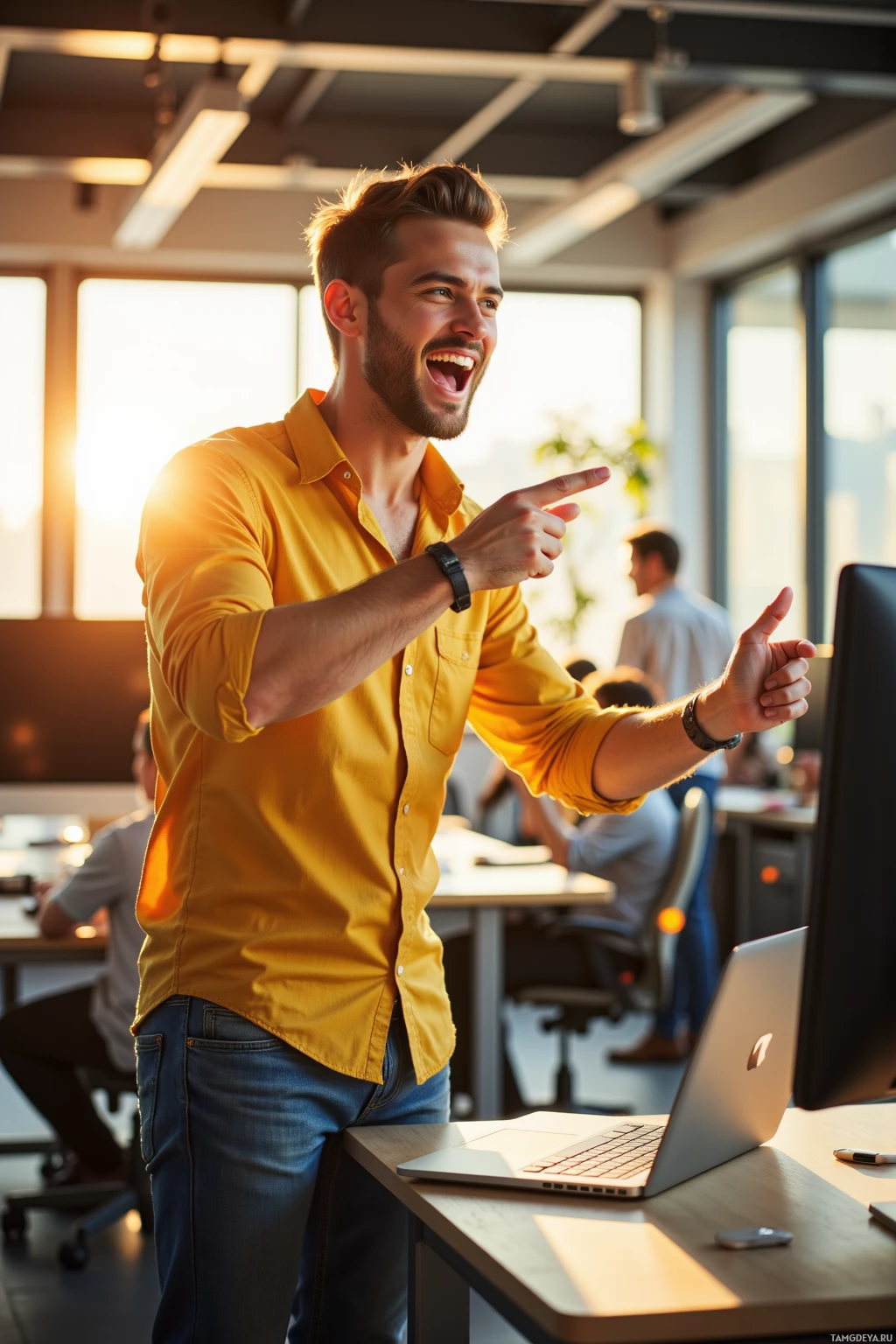 A man in a yellow shirt stands in an office, pointing excitedly towards a computer screen.