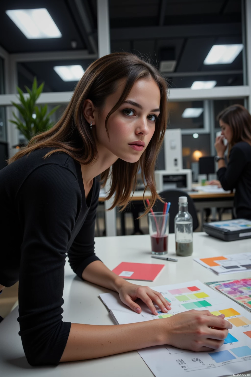Realistic high quality photo. Modern office interior at night: a 30‑year‑old woman with dark brown hair in a sleek low ponytail, deep brown eyes, porcelain complexion, wearing a black fitted top and matching trousers, elegant heels, and a silver watch, hunched over a desk cluttered with a Pantone color sheet, open sketchpad, ink-draining printer, wall clock ticking, her expression tense as she refines the mood board for a spring campaign.